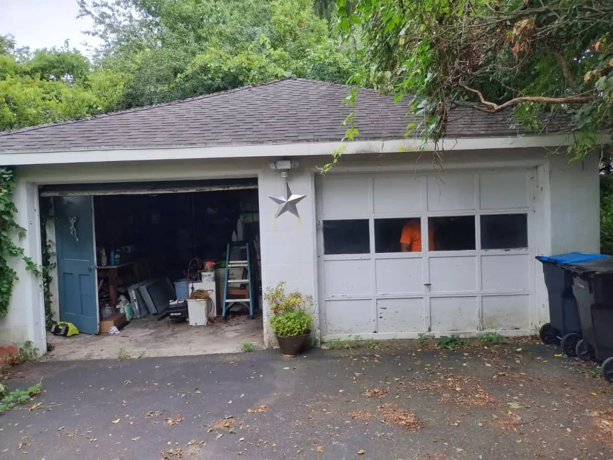 Detached garage with one bay open and one old windowed panel door before replacement
