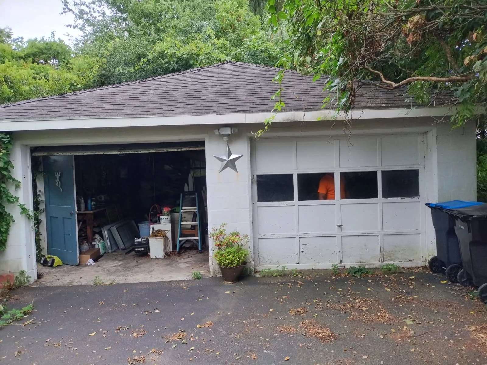 Detached garage with one bay open and one old windowed panel door before replacement