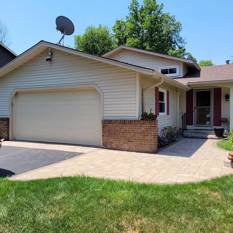 Cream raised-panel garage door on a ranch home with brick accents and paver walkway