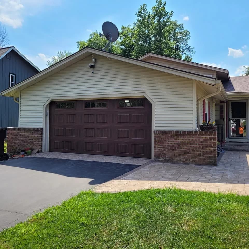 Dark walnut woodgrain garage door with transom windows on a cream home with paver driveway