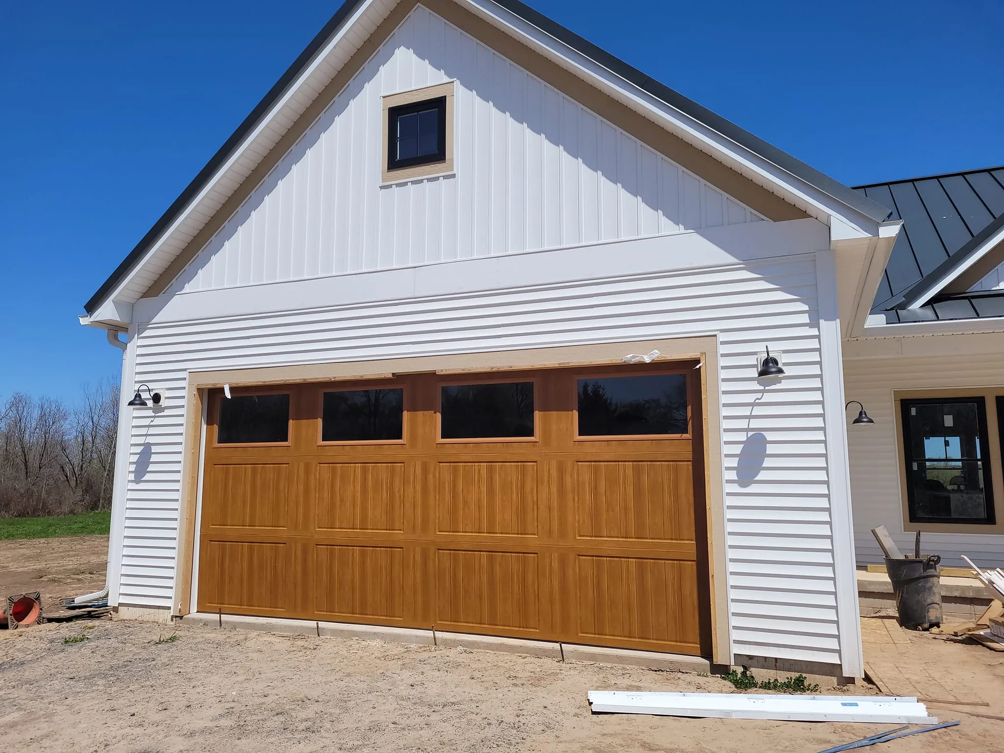 Oak woodgrain carriage-style garage door with large windows on a white farmhouse new construction