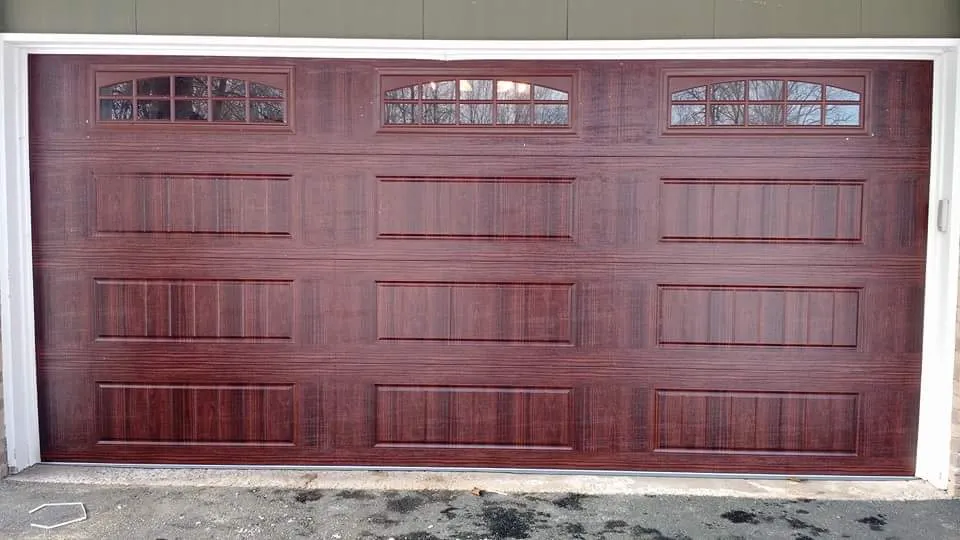Dark wood-grain two-car garage door with arched windows in a cherry finish
