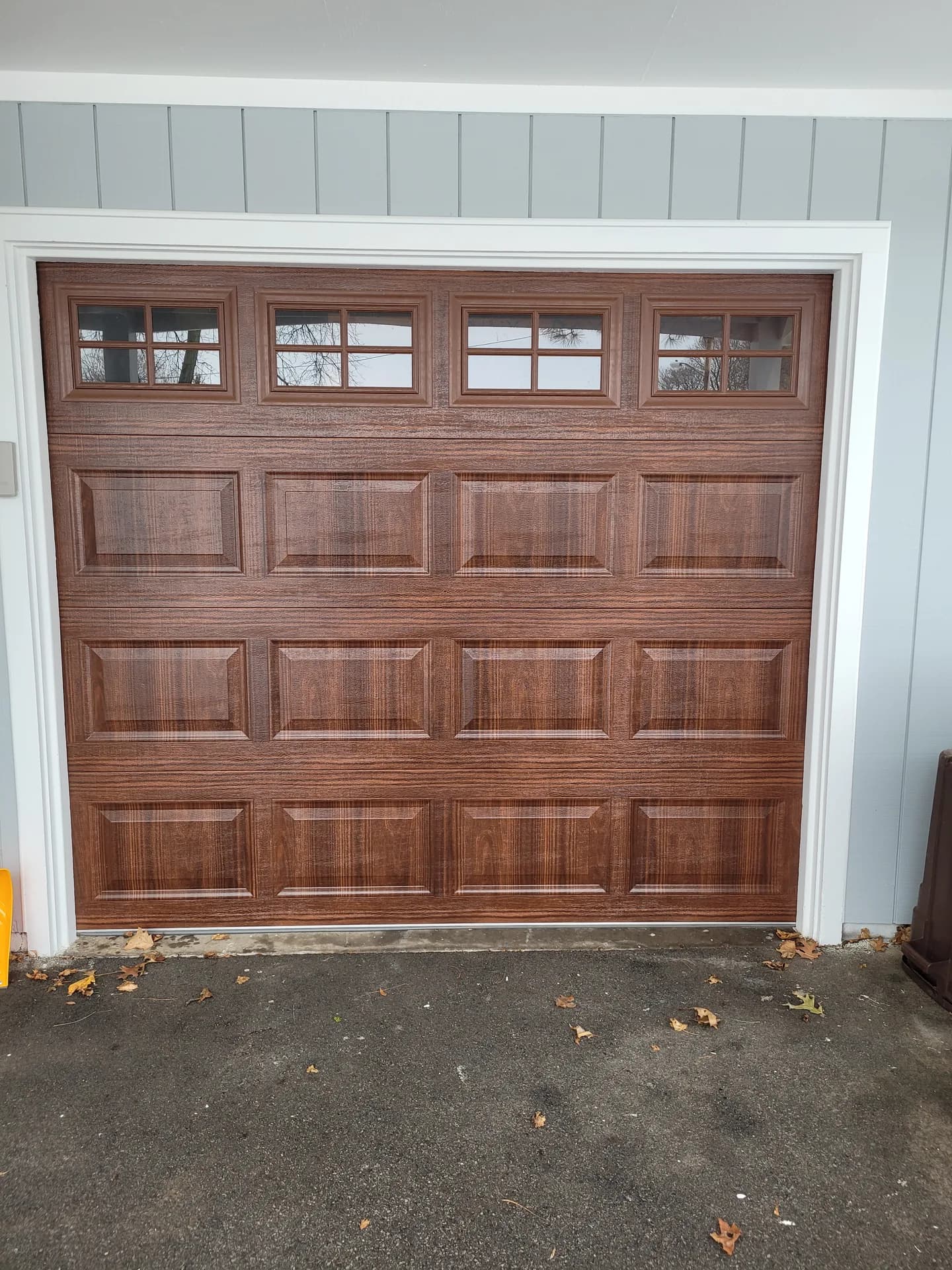 Walnut woodgrain garage door with transom windows on a home with blue-gray board-and-batten siding
