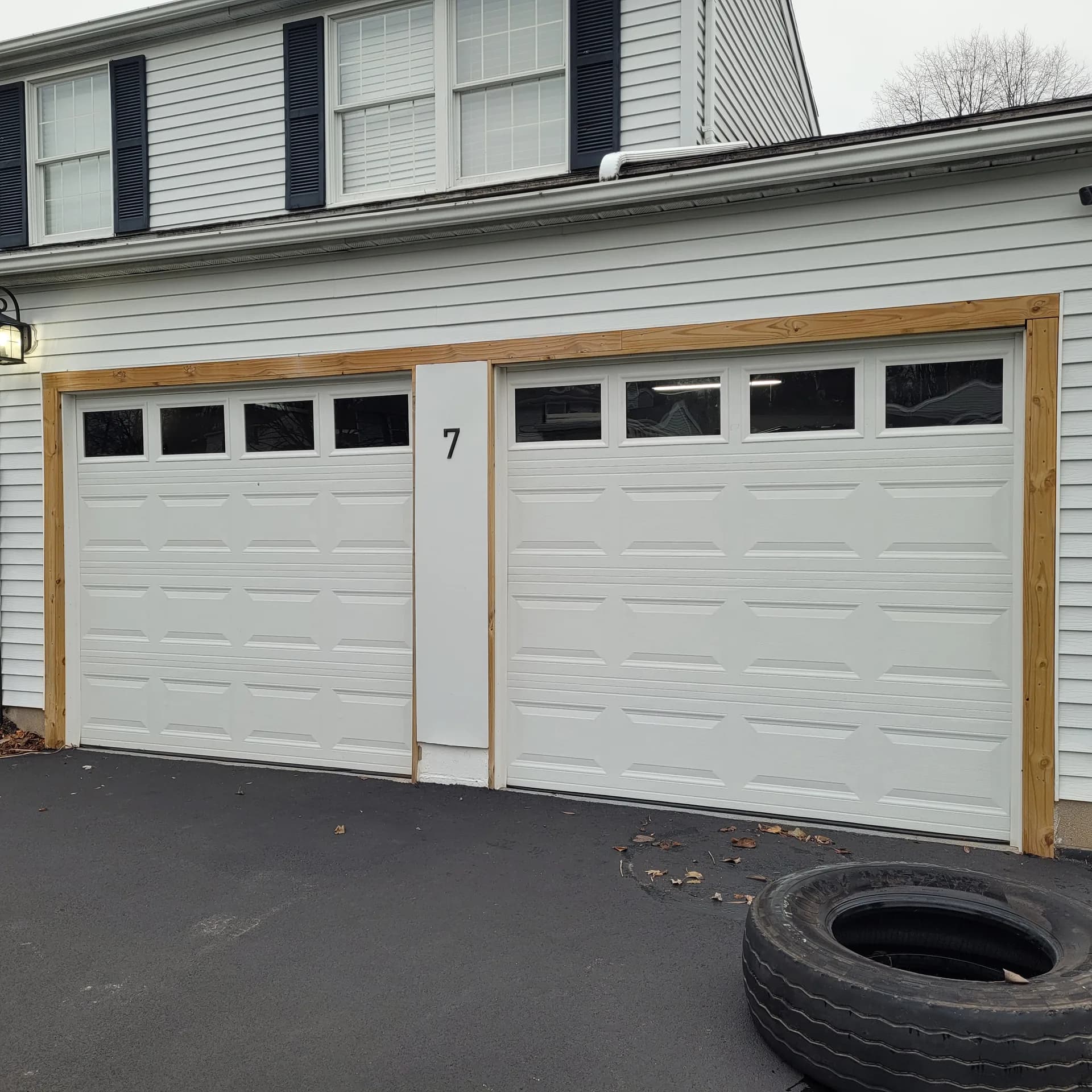 Two white raised-panel garage doors with transom windows and natural wood trim framing