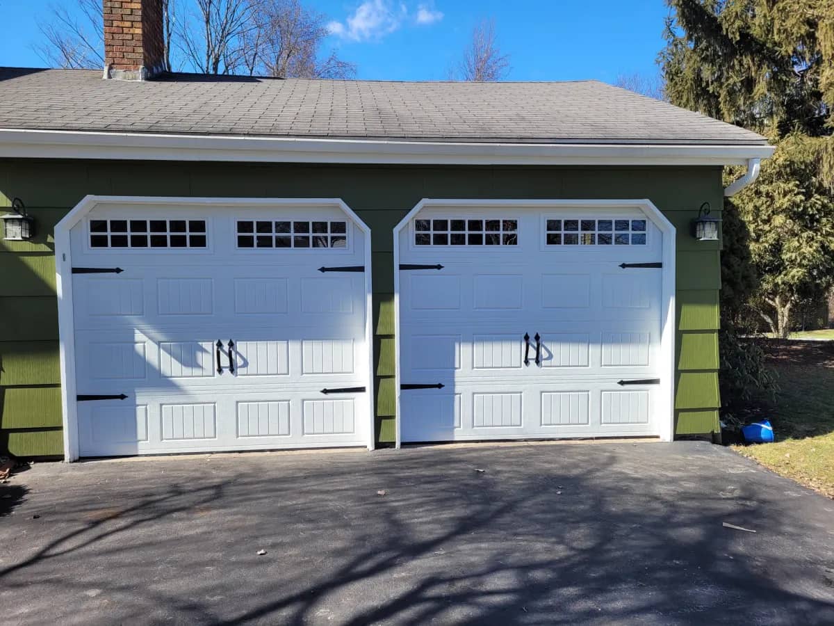 White carriage-style double garage doors on a detached garage with green siding